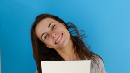  Closeup portrait of beautiful smiling woman with long hair shaking her head, holding blank paper sheet isolated over blue background with copy space. Body language concept. 