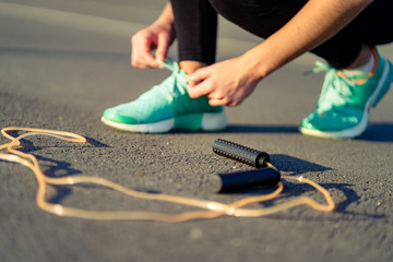 Fitness woman is tying shoelaces on sneakers and is preparing to do cardio exercises with jump rope...