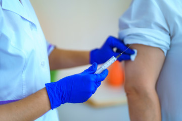 Nurse in gloves making a vaccination in the shoulder patient in hospital room. Flu shot, protection...