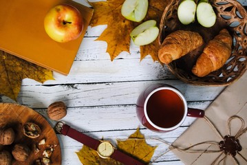 Autumn. A cup of hot tea, croissants apples and walnuts are on the table.