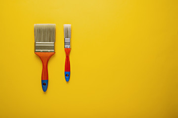 Top view of big and small paint brushes on yellow background with copy space