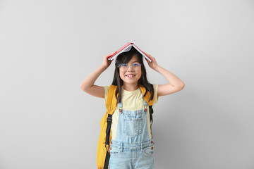 Portrait of happy little schoolgirl with book on light background