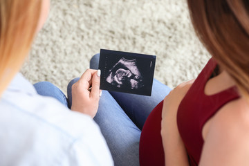 Pregnant lesbian couple with sonogram image at home