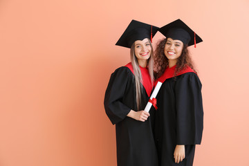 Young students in bachelor robes on color background