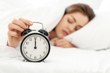 Morning of beautiful young woman with alarm clock in bed