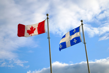 Quebec and Canada flags fluttering in the wind together on blue sky