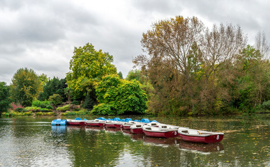Obraz premium Panoramic view of a boating lake with paddle boats parked and park cafe outdoor tables, Battersea Park, London