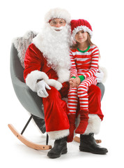 Santa Claus and little girl sitting in armchair against white background
