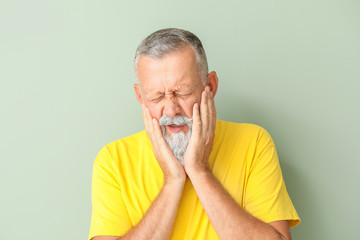Senior man suffering from toothache against color background