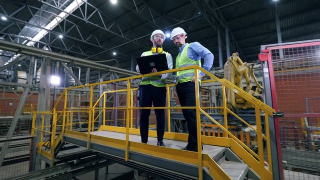 Two engineers are having a discussion in the modern factory with robotic equipment