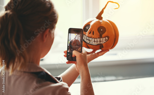 woman artist prepares for halloween and photographed on smartphone his work painted pumpkin.