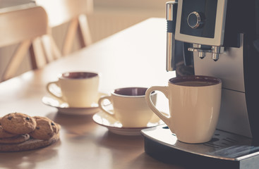 Cups of morning espresso in the coffee machine with biscuits on wooden table