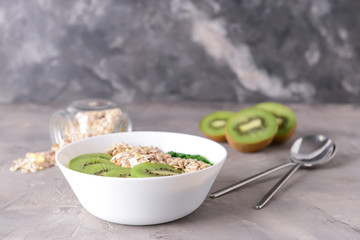 Bowl with tasty oat flakes and kiwi on grey background