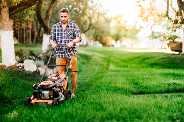 Portrait of young gardener using lawn mower for grass cutting in garden