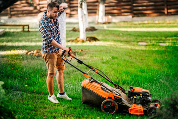 Fototapeta premium Portrait of hard working gardener using lawnmower and cutting grass