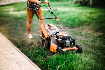 Gardening and landscaping concept - worker, gardener working with lawnmower and cutting grass in garden.