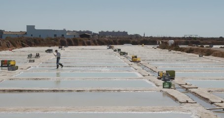 Traditional sea salt production farm, worker preparing evaporation pond. Algarve, Portugal.