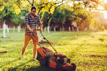 lawncare and landscaping concept - garden maintainance with gardener working and cutting grass