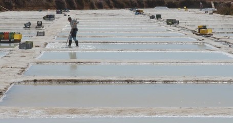 Traditional sea salt production farm, worker preparing evaporation pond. Algarve, Portugal.