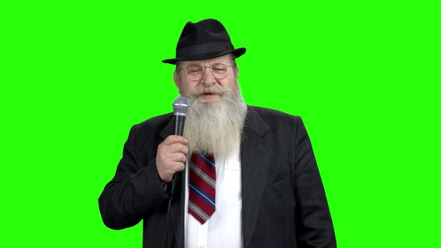 Old businessman with beard talking into microphone. Serious bearded man speaker holding microphone. Green Chroma Key background.