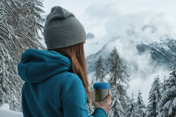 Young girl with a thermo mug standing overlooking Dolomiti mountans. North Italy