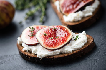 Rye bread toast with figs and ricotta cheese on black slate background, closeup view, selective focus. Healthy food