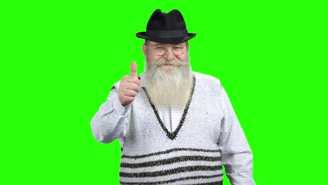 Happy senior man in hat giving thumb up. Portrait of good-looking old man with big beard and smile on green Chroma Key background.