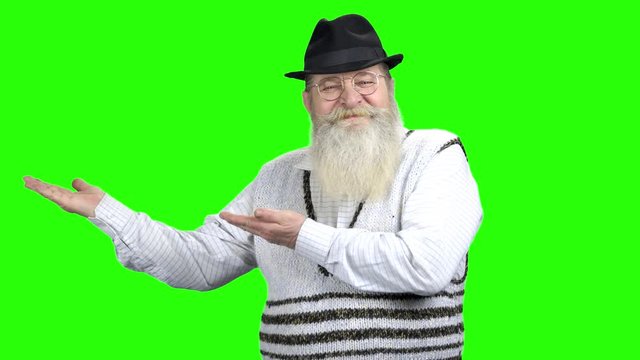 Senior bearded man showing copy space with hands. Happy elderly man in eyeglasses pointing away at copy space on green screen background.
