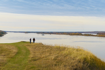 A guy and a girl stand on a high bank of the river and look into the distance on an autumn cloudy day
