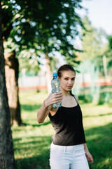Girl athlete with a bottle of water in her hands. Summer sunny day in the park
