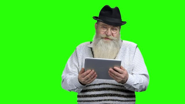 Elderly man in hat holding computer tablet. Smiling senior man with beard doing video call on Alpha Channel background. The older generation and modern technology.