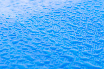 Close up of several dew drops on top of a blue car