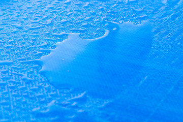 Small puddle beside some raindrops on top of a car on a blue surface