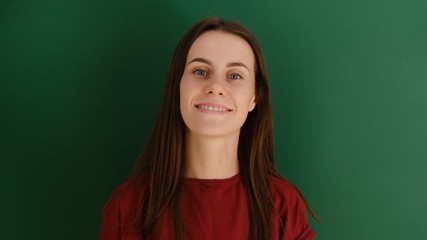 Beautiful young woman with flying hair smiling and looking at he camera with raised hands, posing over green background. Charming brunette female with beautiful long hair