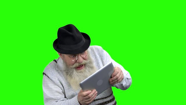 Enthusiastic pensioner playing game on tablet pc. Old caucasian man immersed into gaming. The older generation and modern technology. Green Chroma Key background.