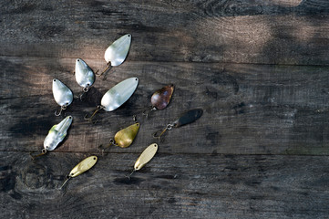 Metal spinners in the shape of a spoon of different colors for catching a predator on a vintage wooden background.