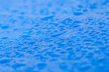 Close up of rain water drops on the surface of a blue car