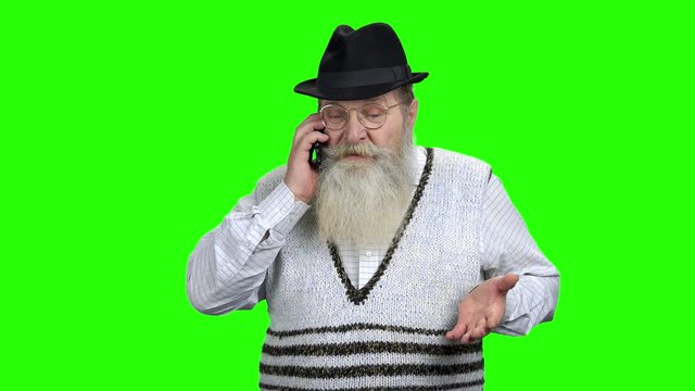 Angry senior man talking on mobile phone. Aged man arguing or having dispute with another person on cellphone. Green Chroma Key background.