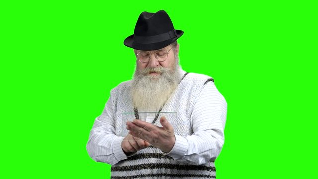 Caucasian pensioner using glass digital tablet. Aged man with long beard wearing black hat. Green screen background.
