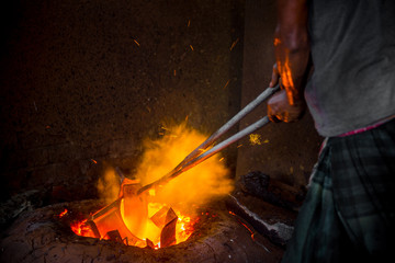 Unsafe worker hands. A local steel machine parts making yard worker melting scrap on hot furnace.