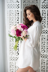 Healthy pregnancy and happy motherhood. Beautiful young pregnant woman with a bouquet of flowers on the background of an openwork wooden carved screen.