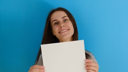  Closeup portrait of beautiful smiling woman with long hair shaking her head, holding blank paper sheet isolated over blue background with copy space. Body language concept. 