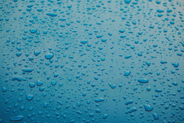 Close up of raindrops, water drops on a polished blue metal surface for background purpose. Selective focus