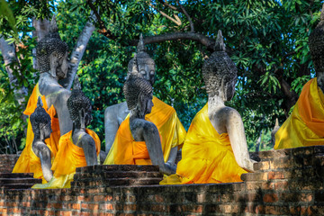Some buddha statues sit with orange robes facing a temple in Chaimongkhon Thailand