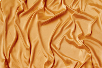 gold beautiful satin fabric draped with soft folds, silk cloth background, close-up, copy space