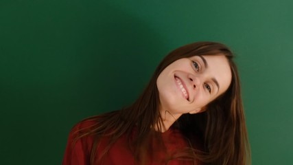 Young pretty girl with long hair smiling shaking her head isolated over green background. Charming brunette female with beautiful long hair