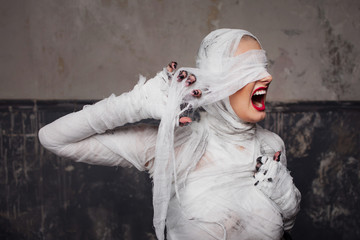 Screaming mummy rips bandages. Portrait of a young beautiful woman in bandages all over her body.