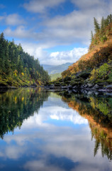 Nearly perfect fall reflections with blue sky and fluffy white clouds while rafting down the Rogue River in Oregon.
