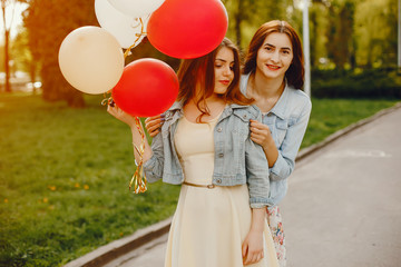 two young and bright girls spend their time in the summer park with balloons © hetmanstock2
