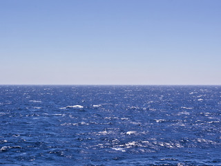Wavy deep blue sea and sky. Horizon line in the middle of the frame.
